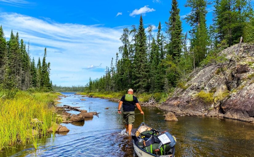 A man pulling a canoe in the water that is full of camping gear.