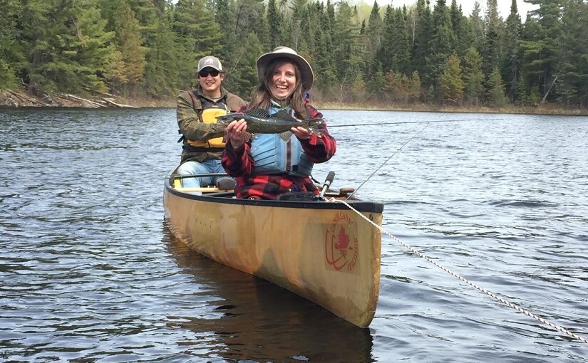 Two people in canoe hold up a fish.